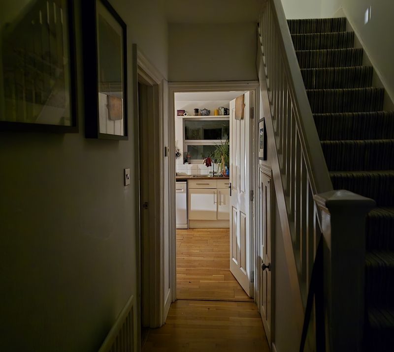 The interior of a house in semi-darkness. A light in kitchen. Some stairs.